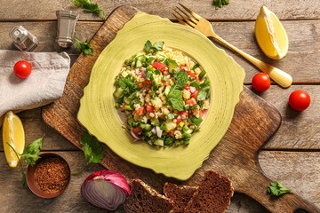 Plate with delicious tabbouleh salad and spices on wooden background