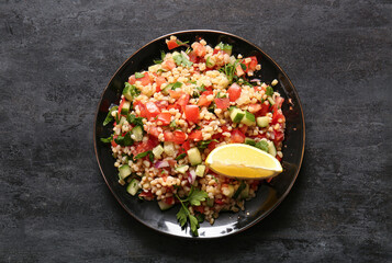 Plate with delicious tabbouleh salad on black background