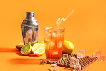 Glass of tasty Long Island iced tea, citrus fruits, shaker and ice cubes on color background