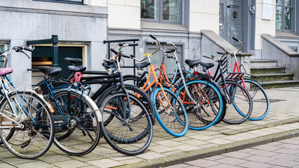 Fototapeta na wymiar Bike parking in the city. Bicycle parking along a street near a city building in Amsterdam. An urban cityscape with bicycles. Walking bikes parked casually along an old street in Netherlands.