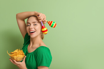 Pretty young woman with nachos and maracas on green background