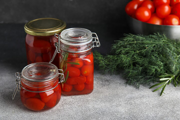 Jars of pickled tomatoes with rosemary and dill on grey table