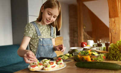 Girl preparing sandwiches with avocado, tomatoes cherry and greens at kitchen. Vegetarian bruschettas and salad with fresh vegetables and arugula