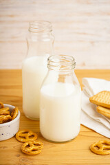 Milk in jug with cookie on wooden table and light background, vertically, close-up.