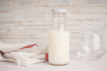Milk in jar and glass on a light wooden background.