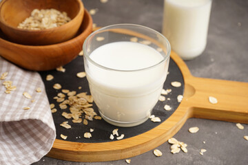 Oat milk in the glass with jug of milk and oat on a wooden background.