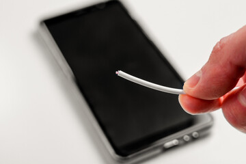Hand holding a broken torn charger cable with a black smartphone on a white background