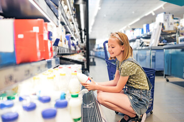 Pretty girl child choosing milk in supermarket shop. Beautiful female preteen kid looking lactose...