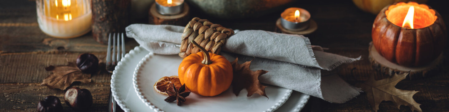 Atmospheric autumn elegant beautiful table setting with pumpkins for a wedding or thanksgiving family celebration. Fall decoration countryside rustic style, cozy home atmosphere , candles, wine banner