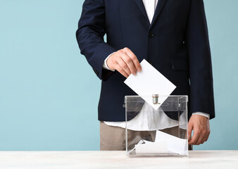 Voting young man near ballot box on blue background, closeup
