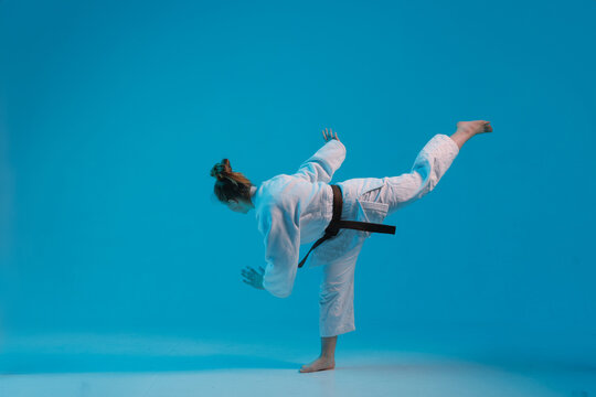 girl judoka in a white kimano with a black belt on a blue background, studio photo
