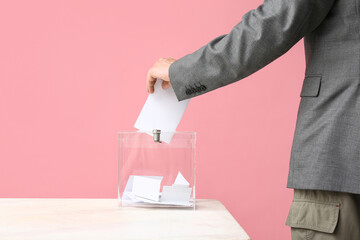 Voting young man near ballot box on pink background, closeup