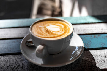 Cappuccino Tassen aus Porzellan in einem Café bei Sonnenschein auf einem Holztisch im Freien mit Herzsymbol