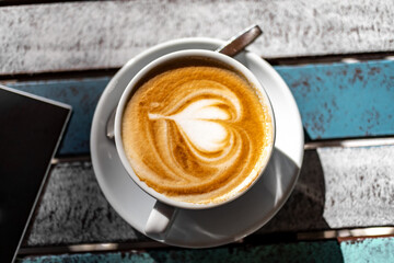 Cappuccino Tassen aus Porzellan in einem Café bei Sonnenschein auf einem Holztisch im Freien mit Herzsymbol