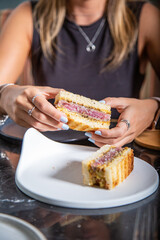 Sandwich de tartar de carne de lomo alto de ternera con salsa en pan tostado, tomado por manos de chica con las uñas pipntadas en la mesa de un restaurante  - obrazy, fototapety, plakaty