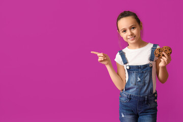 Cute little girl with cookies pointing at something on purple background