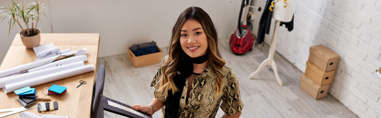 joyful asian stylist with color swatches smiling at camera in private atelier, horizontal banner