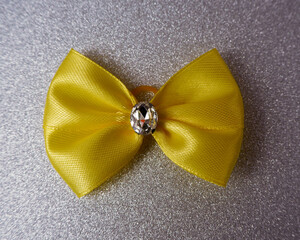 On a gray shiny background lies a yellow bow with a shiny stone in the middle, attached to a latex...