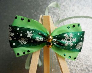 Close up on a gray background on a wooden stand there is a green satin bow with snowflakes with stones for dogs. pet accessories for christmas. front view
