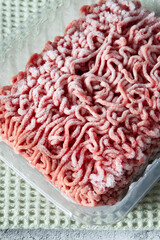 Frozen beef steak mince in a plastic container defrosting. On a green tea towel.