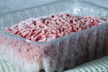 Frozen beef steak mince in a plastic container defrosting. On a green tea towel.