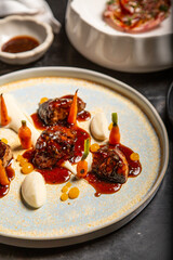 Chef decora un plato de carne a la parrilla con salsa glaseada en un plato con zanahorias salsa de almendras, reducción de yema de huevo y perlas de crema en una mesa de restaurante de marmol negro 
