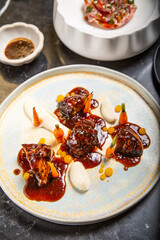 Chef decora un plato de carne a la parrilla con salsa glaseada en un plato con zanahorias salsa de almendras, reducción de yema de huevo y perlas de crema en una mesa de restaurante de marmol negro 