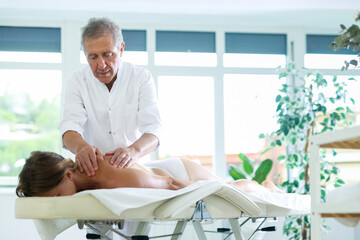 Mature masseur doing back massage procedure for woman patient in therapy cabinet
