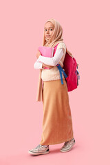 Little Muslim girl in hijab with school backpack and books on pink background