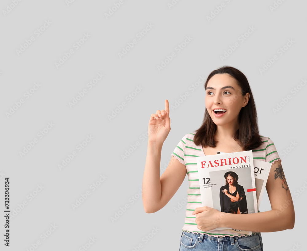 Poster beautiful woman with magazines pointing at something on light background