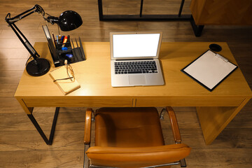 Workplace with blank laptop, stationery and glowing lamp in office at night, top view