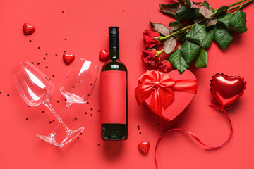 Bottle of wine with glasses, roses and gift on red background. Valentine's Day celebration