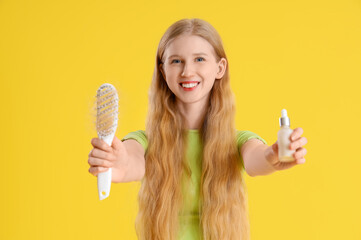 Young woman with brush and serum for hair growth on yellow background