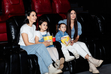 Little girls, friends with their moms watching a cartoon film at a movie theater, house or cinema....