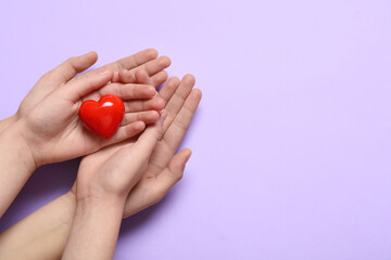 Hands of woman and child with red heart on lilac background
