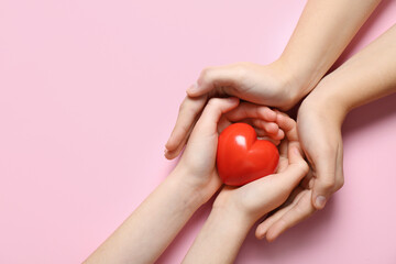 Hands of woman and child with red heart on pink background