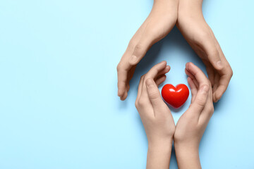 Hands of woman and child with red heart on blue background