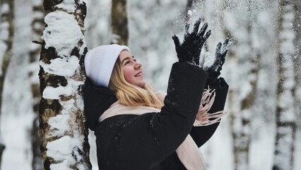 A girl is walking through the woods and kicking up snow in a birch forest.