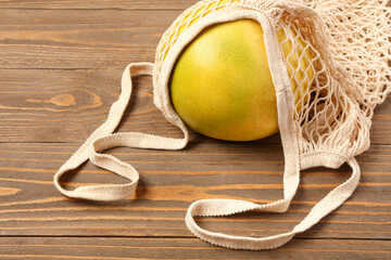 Fresh juicy pomelo in string bag on wooden table