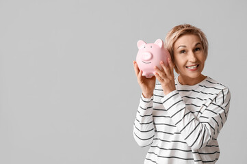 Happy mature woman with piggy bank on grey background