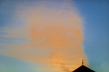 Orange-coloured cloud formation in the blue morning sky above the spire of St. Albert's Church in Augsburg