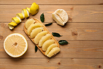 Board with pieces of fresh pomelo fruit and leaves on wooden background