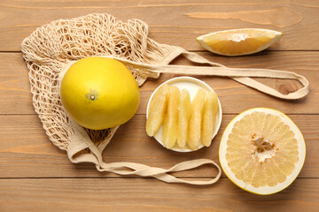 String bag and plate with pieces of fresh pomelo fruit on wooden background