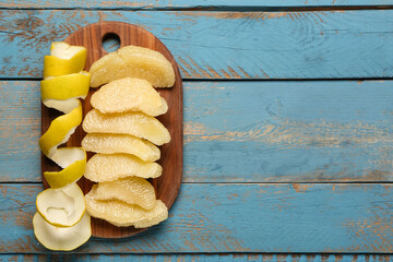 Board with pieces of fresh pomelo fruit on blue wooden background