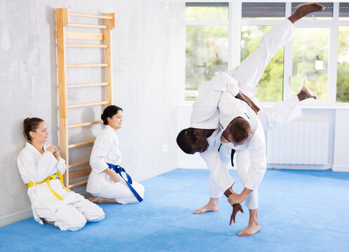 Practiced middle-aged male jujutsu practitioner demonstrating throw method on his partner in sports hall