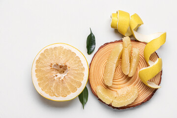 Wooden board with pieces of fresh pomelo fruit and leaves on white background