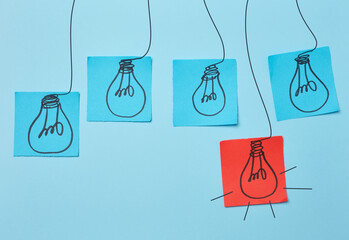 Drawn electric lightbulbs on paper sheets with a blue background, signifying the concept of...