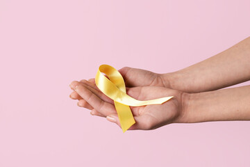 Hands with golden ribbon on pink background. Childhood cancer awareness concept