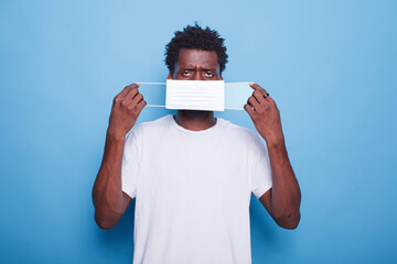 Portrait of black guy putting on face mask to protect himself from coronavirus epidemic. African...