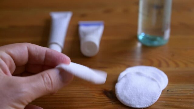 Close-up image footage on a cotton pad for cleaning and skin care. The hand grabs one, in the background a bottle of micellar water and a tube of skin care cream.